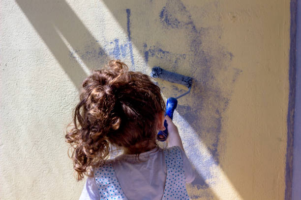 istock Little kid girl paints wall by paint roller 860045552