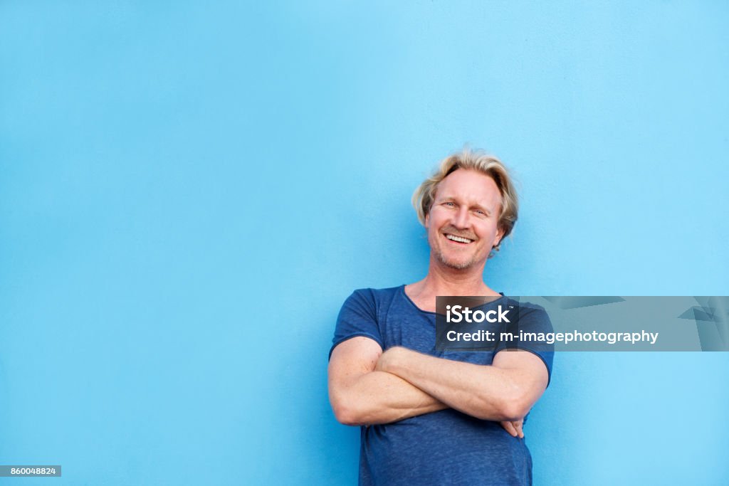 souriant le milieu d’ans homme posant avec les bras croisés - Photo de Fond bleu libre de droits