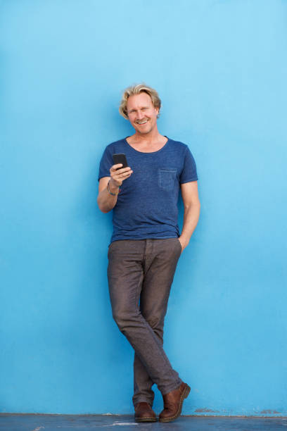 istock Full body happy man standing by wall with mobile phone 860048948