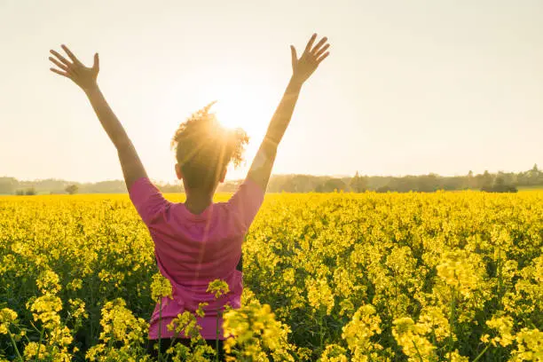 Photo of Mixed race African American girl female young woman athlete runner teenager in golden sunset or sunrise arms raised celebrating in field of yellow flowers
