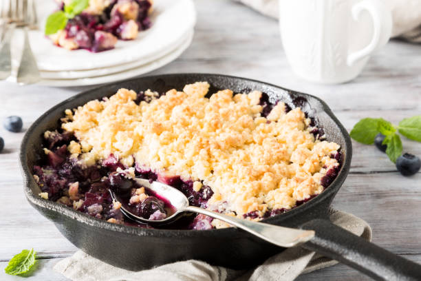 Coconut crumble in cast iron pan Coconut crumble in cast iron pan with fresh apples and blueberry. Healthy food concept. cobbler dessert stock pictures, royalty-free photos & images