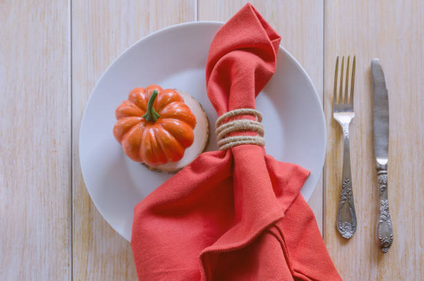 istock Thanksgivings Day festive background. Beautiful autumn table settings for thanksgiving dinner: white plate with small pumpkin and orange linen napkin with vintage cutlery. Top view. 860053366