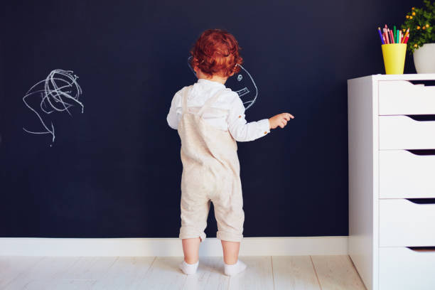 carino bambino rossa disegno sul muro di gesso a casa - back against the wall foto e immagini stock