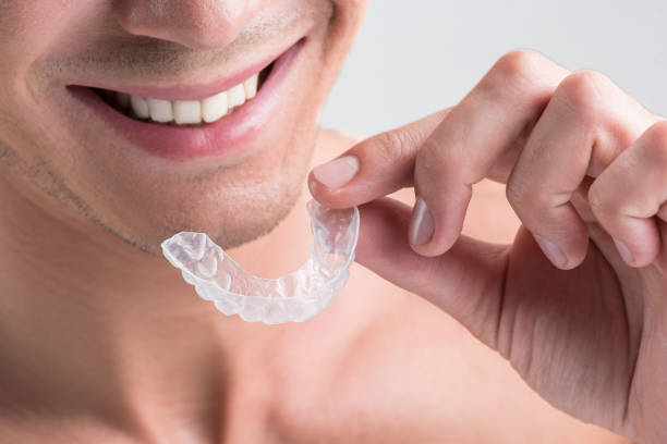 Cheerful young nude guy is holding plastic transparent brace Straight teeth. Close-up of male hand with clear aligner for orthodontic correction of bite. Man is smiling. Isolated background dental aligner photos stock pictures, royalty-free photos & images