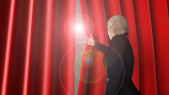 woman looking through theatre curtains on stage.