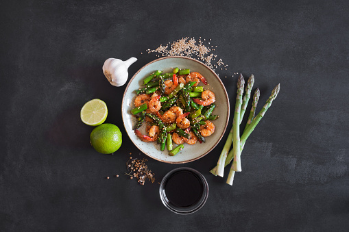 Asian salad with asparagus and shrimps in plate on the black background