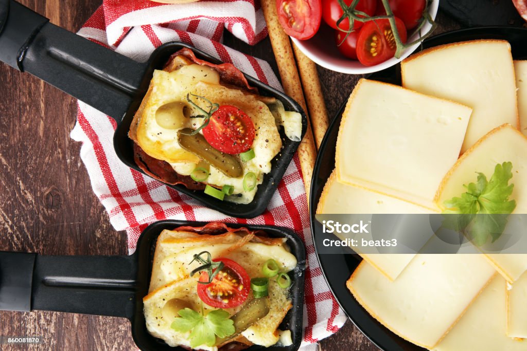 Suiza tradicional delicioso derretido queso raclette en cubitos patata hervida o al horno servido en cazuelas individuales con salami - Foto de stock de Raclette libre de derechos