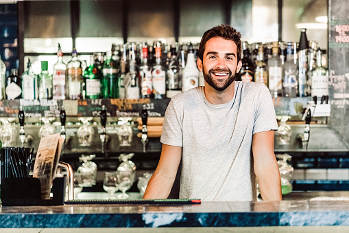 Portrait of smiling bartender. Man is wearing casuals. He is standing at bar counter.