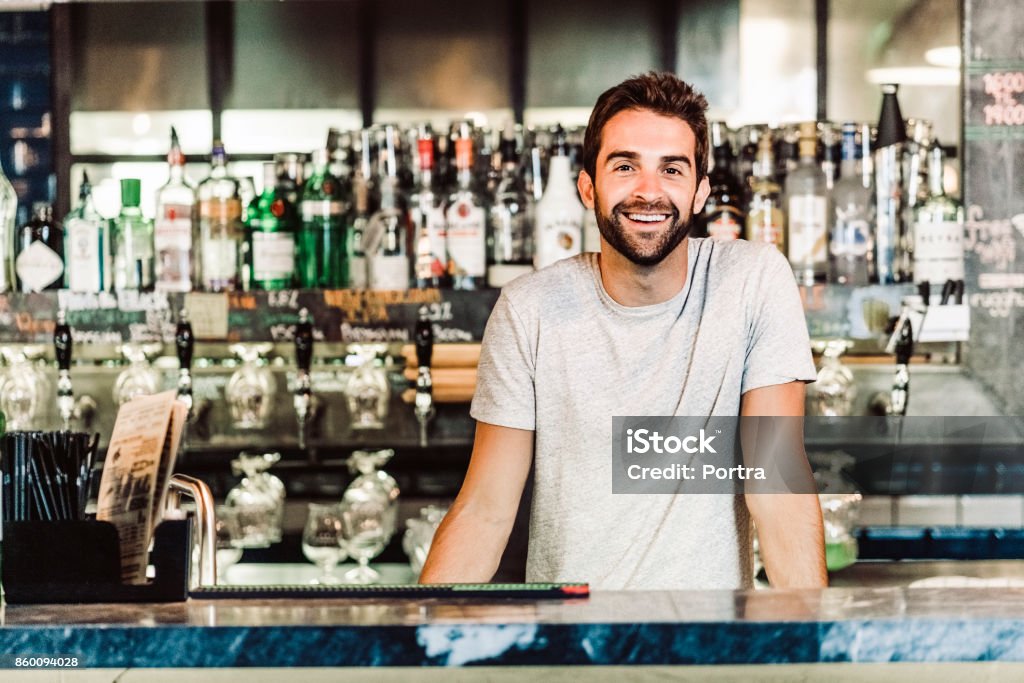 Portrait of bartender standing at bar counter Portrait of smiling bartender. Man is wearing casuals. He is standing at bar counter. Bartender Stock Photo