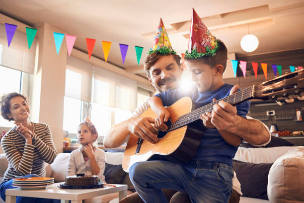 father plays guitar with his son and celebrating birthday happy young family celebrating a birthday and having fun together father and son guitar stock pictures, royalty-free photos & images