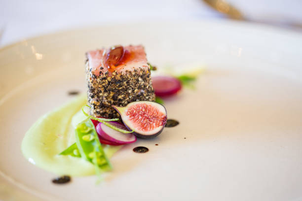 Close up of a gourmet pork dish covered in crushed black pepper with sweet green figs on the side