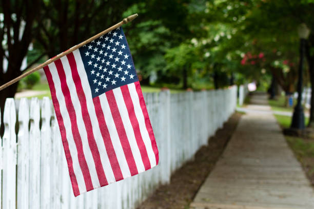American Flag on a Picket Fence Small American flag hangs from a picket fence along the sidewalk in a rural town. sidewalk photos stock pictures, royalty-free photos & images
