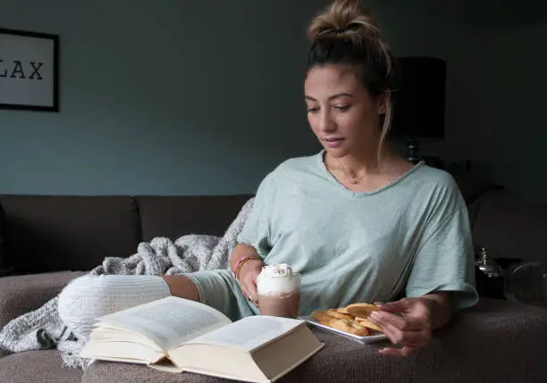 closeup of beautiful young mixed race, Asian - Caucasian, woman reading book at home on couch with hot chocolatemilk and cookies