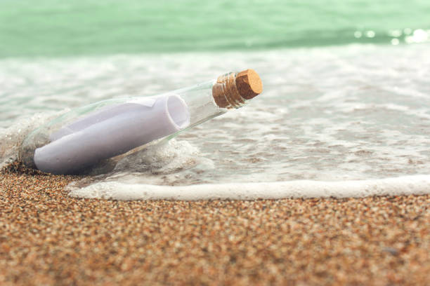 istock Message in a glass bottle on the sand. Sea and waves. A note on salvation, please help 860113488