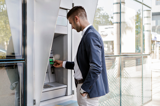 Businessman holding card at an ATM ready to withdraw cash