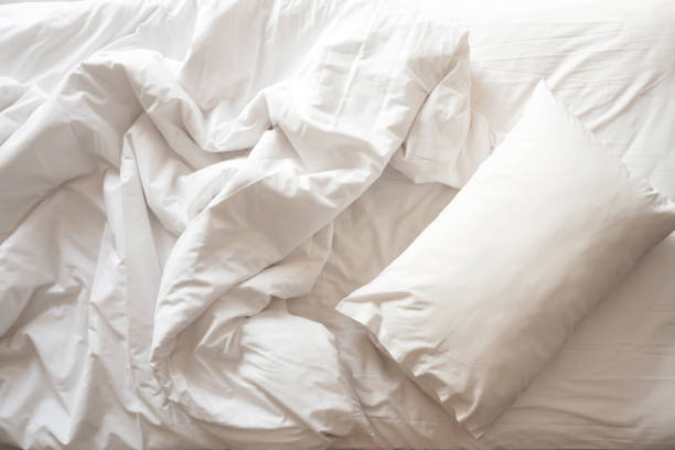 Messy bed. White pillow with blanket on bed unmade. Top view. Messy bed. White pillow with blanket on bed unmade. Concept of relaxing after morning. With lighting window. Top view. duvet stock pictures, royalty-free photos & images