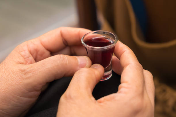 mãos de uma mulher segura um copo de vinho vermelho em comunhão. - grail - fotografias e filmes do acervo