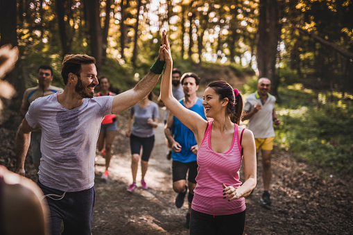 Happy marathon runners giving each other high five while running a race in the forest.