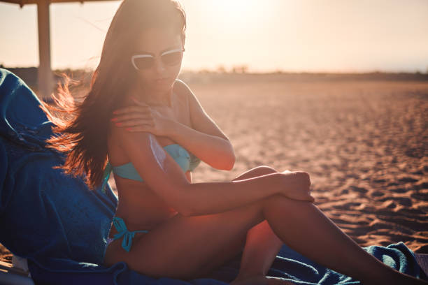 fille, appliquer la crème tout en étant assis sur la plage solaire - outdoor chair beach chair umbrella photos et images de collection