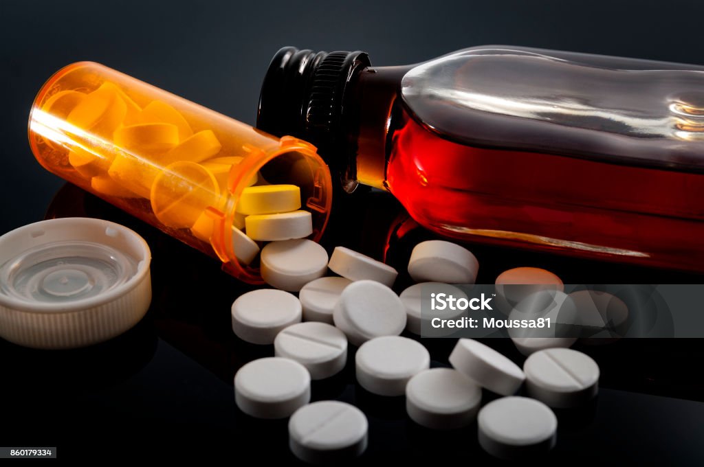 Spilled opioids and a flask of hard liquor Opioid epidemic, drug abuse and dangerous mixing of barbiturates and alcohol concept with oxycodone pills fallen out of a prescription pill bottle next to a flask of hard liquor Alcohol - Drink Stock Photo