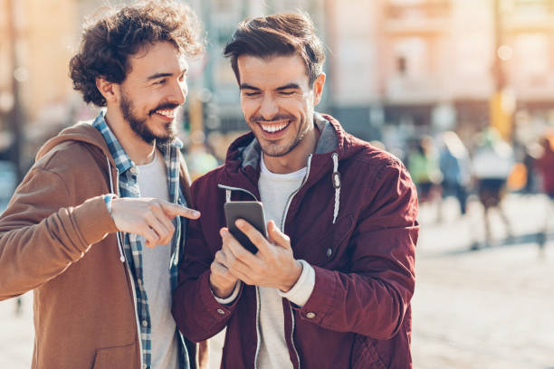 Two young men having fun Two young men looking at a smart phone and laughing outdoors in the city street friends stock pictures, royalty-free photos & images