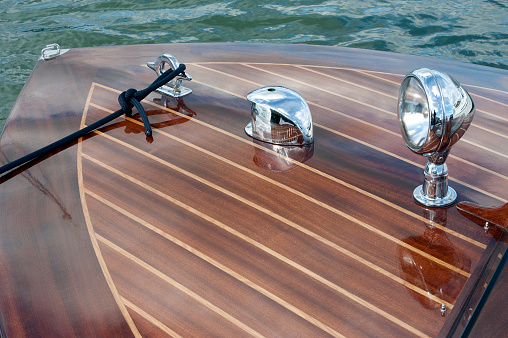 The foredeck of Panther with chrome fittings of headlight, navigation light and mooring cleat - a pristine classic gentlemans highly polished wooden powerboat, reminiscent of the nineteen twenties art deco style of a bygone era, in Poole Harbour, England, UK