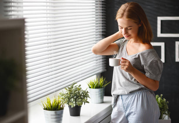 istock happy young woman   drinks coffee at window in morning 860206770