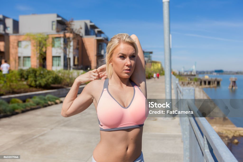 Young blonde woman stretching outside before jogging A beautiful blonde jogger stretches her arms before goes for a run along the river.  She has her left arm bent behind her neck and is grasping it with her right hand. 20-29 Years Stock Photo