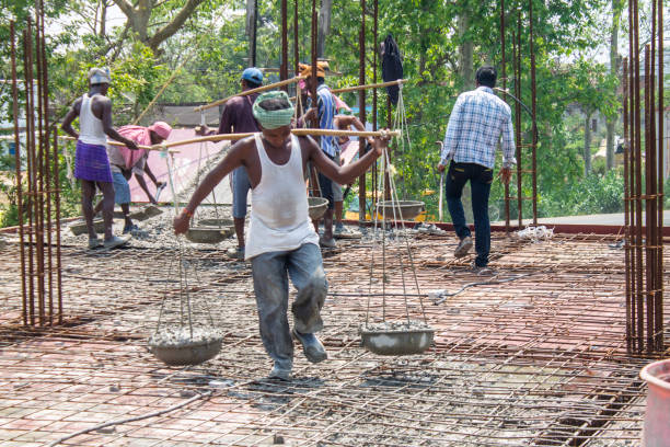 Rural construction workers on site Bargarh, India- 08-4-2015: A Indian construction worker transporting concrete on big balancing scale like container. All the construction workers in India work witout any safety gear and with very primitive tools. grill rods stock pictures, royalty-free photos & images