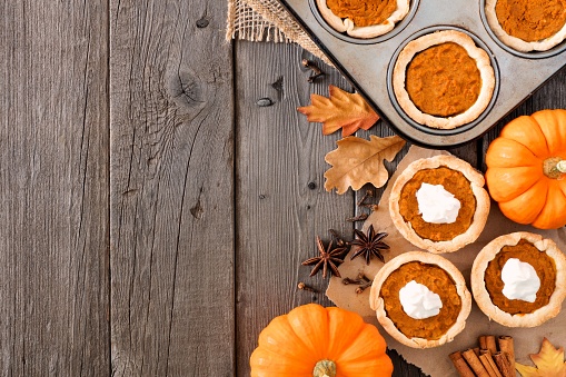 Autumn baking scene side border with pumpkin tarts over a wood background