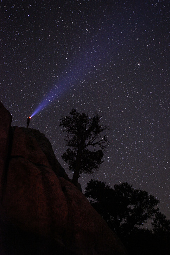 A hiker standing on a cliff with headlamp shining to the starry night sky