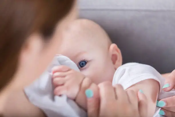 Cute baby looks up at her mother while breastfeeding. One of the baby's blue eyes is looking at her mom.