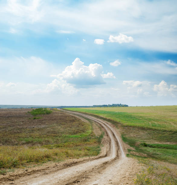 istock dirty road in field and blue sky with clouds 860261350