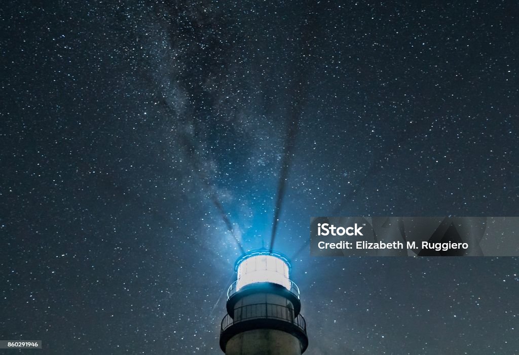 Lighthouse at night with radiating beams and starry sky with Milky Way Top part of New England lighthouse isolated against dark, starry sky, with light beams radiating upward Lighthouse Stock Photo