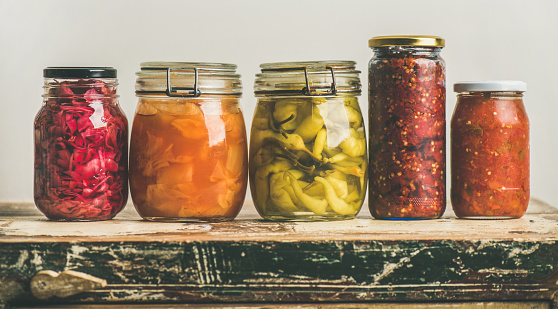 Autumn seasonal pickled or fermented vegetables in jars placed in row over vintage kitchen drawer, white wall background, copy space. Fall home food preserving or canning