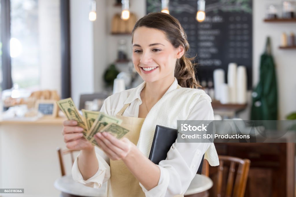 Happy waitress is pleased after receiving a large tip Cheerful young female Hispanic waitress smiles while counting out a large tip. Currency Stock Photo