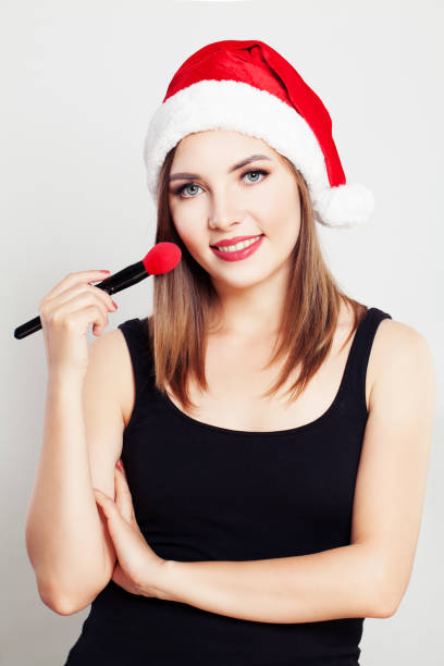 Smiling Woman Makeup Artist wearing Christmas Santa Hat Smiling Woman Makeup Artist wearing Christmas Santa Hat lieke klaus stock pictures, royalty-free photos & images