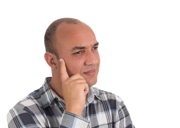 Latin American observes something and has an expression of doubt on his face. He is bald and wears plaid shirts.