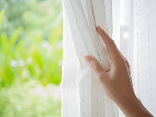 tende aprimani per donna in camera da letto con luce naturale e sfondo giardino. - curtain window women opening foto e immagini stock