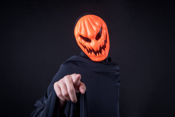istock Mystery man with orange pumpkin evil mask pointing hand on black background 860338018