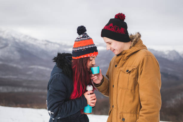 couple drink hot tea from thermos at winter. mountains in snow at background - sexual issues sexual activity couple tan imagens e fotografias de stock