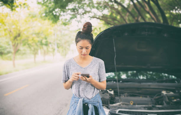 asian woman using mobile phone while looking and stressed man sitting after a car breakdown on street - roadside emergency imagens e fotografias de stock