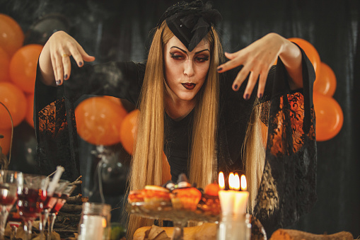 Young woman dressed as vampire is at the Halloween buffet, getting ready to eat delicious cupcakes and have her favorite drink.