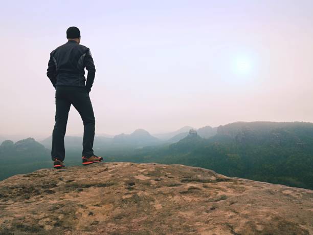istock Nature hiker on sharp cliff roc watching over misty  valley to blurred horizon. Terrible rainy weathe 860384122