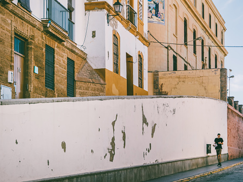 Cadiz, Spain - September 15th, 2017: Local walks down a cobble street  in the background through a mixed commercial and residential district in Cadiz,Spain. Cadiz is considered to be the oldest city in Western Europe.