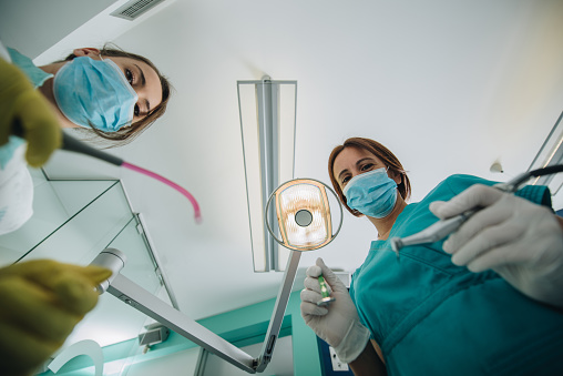 Below view of female dentist and her assistant examining teeth at dentist office.