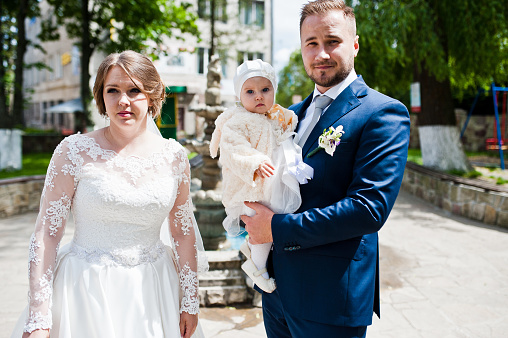 Wedding couple posing outdoor with their small daughter on their wedding day.