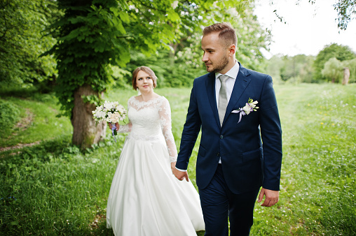 Amazing wedding couple walking and posing somewhere in the green meadow in spring.