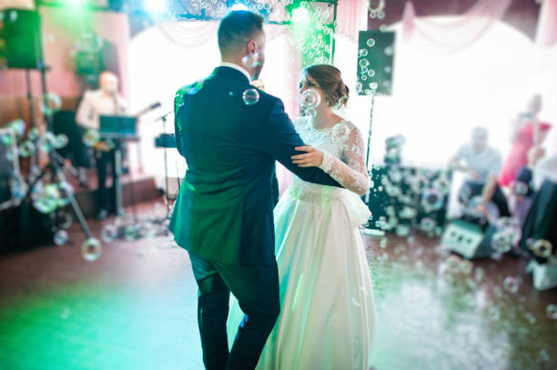 istock Beautiful wedding couple performing their first dance in the restaurant with different lights and bubbles and guests on the background. 860459234