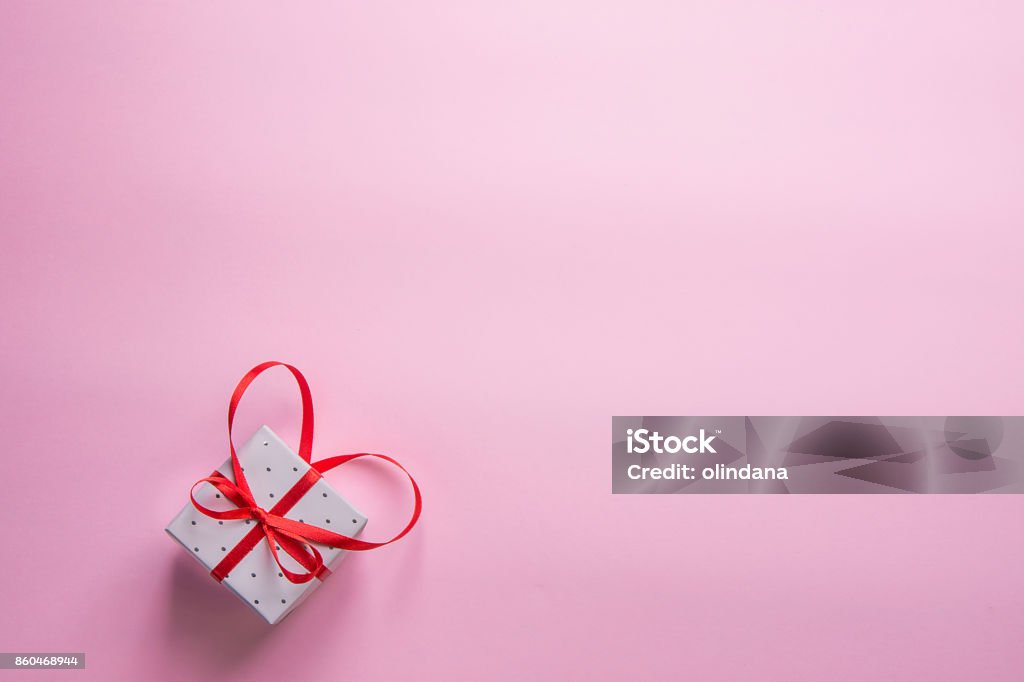 Elegant Gift Box Tied with Red Ribbon with Bow in Heart Shape on Pink Background. Valentine Wedding Mother's Day Birthday Women. Copy Space. Greeting Card Poster Template. Birthday Stock Photo